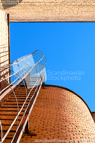 Image of Industrial ladder, blue sky and brick walls of the building