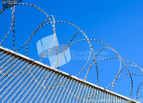 Image of Fence with a barbed wire against the blue sky. 