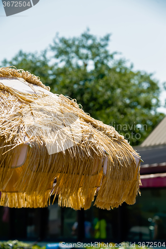 Image of Straw beach umbrella on blue sky background