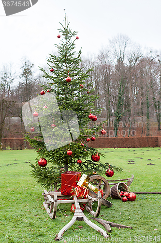 Image of Old wooden frame a sledge with Christmas parcels before a decorated Christmas tree