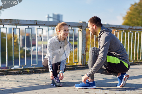 Image of smiling couple tying shoelaces outdoors