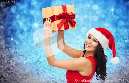 Image of happy woman in santa hat with gift over glitter