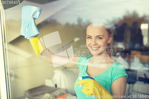 Image of happy woman in gloves cleaning window with rag