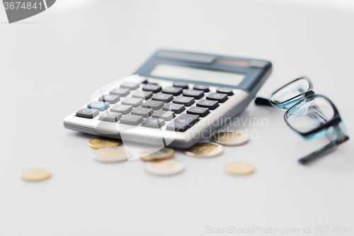 Image of calculator, eyeglasses and coins on office table