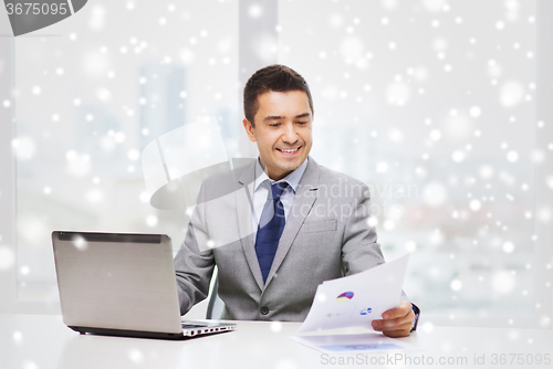 Image of smiling businessman with laptop and papers