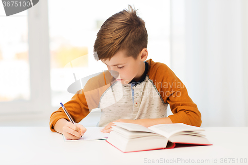 Image of student boy with book writing to notebook at home