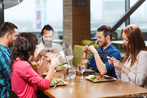 Image of happy friends taking picture of food at restaurant
