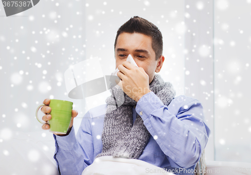 Image of ill man with flu drinking tea and blowing nose