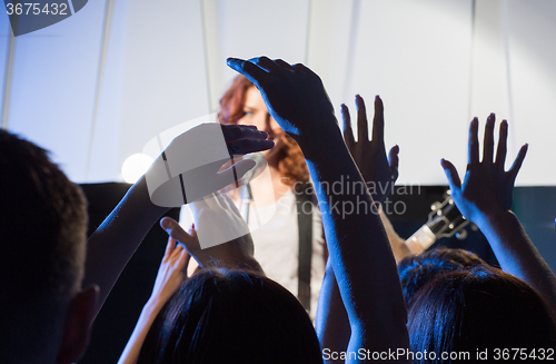 Image of female singer with guitar over happy fans hands