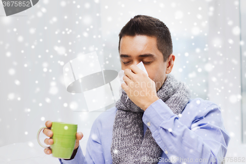 Image of ill man with flu drinking tea and blowing nose