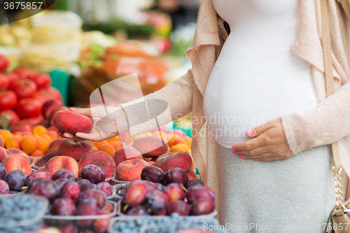 Image of pregnant woman choosing fruits at street market