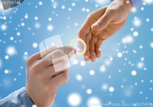 Image of close up of male gay couple hands giving condom