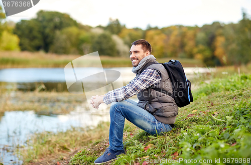 Image of smiling man with backpack resting on river bank