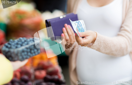 Image of pregnant woman with wallet buying beries at market