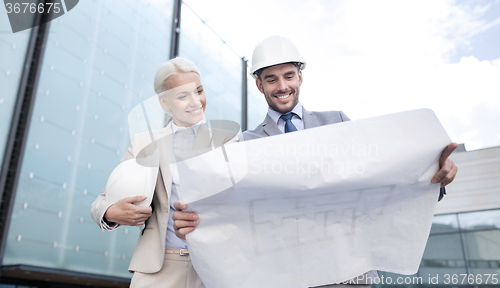 Image of smiling businessmen with blueprint and helmets