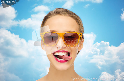 Image of happy young woman in sunglasses showing tongue