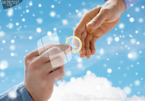 Image of close up of male gay couple hands giving condom