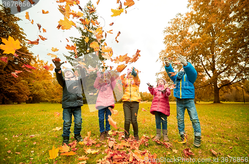 Image of happy children playing with autumn leaves in park