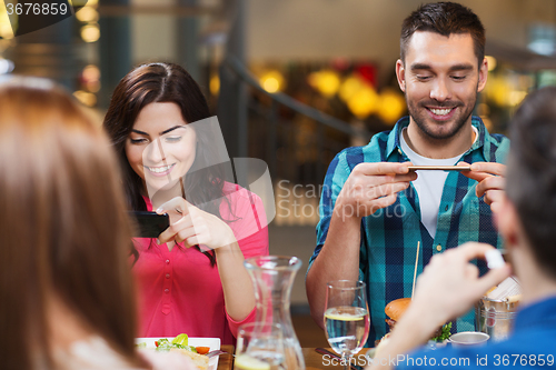 Image of happy friends taking picture of food at restaurant