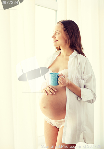 Image of happy pregnant woman with cup drinking tea at home