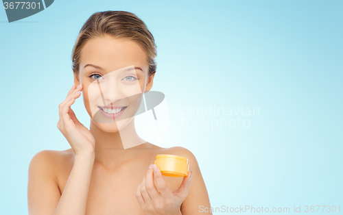 Image of happy young woman applying cream to her face