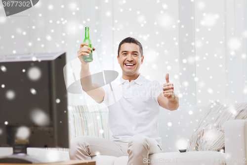 Image of smiling man watching tv and drinking beer at home