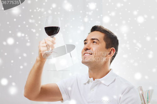 Image of happy man drinking red wine from glass at home