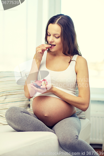 Image of happy pregnant woman eating fruits at home