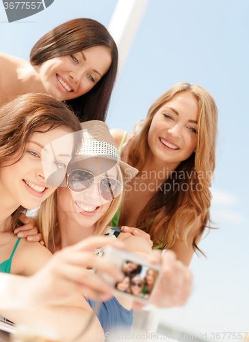 Image of smiling girls taking photo in cafe on the beach