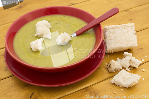 Image of Torn pieces of bread on green pea and ham soup in a red bowl