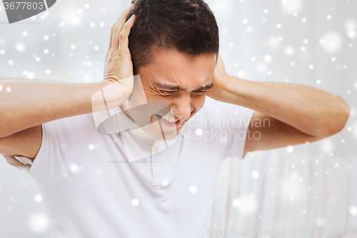 Image of unhappy man closing his ears by hands at home