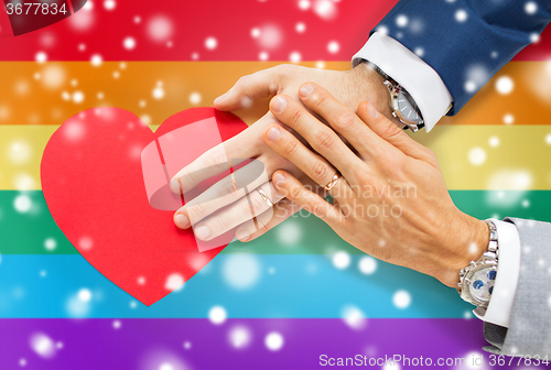 Image of close up of male gay couple hands with red heart