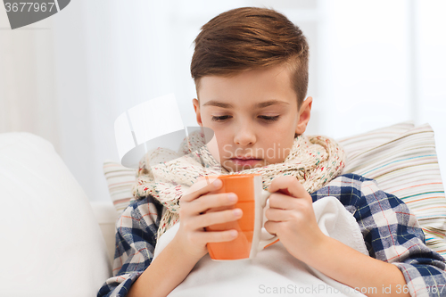 Image of ill boy with flu in scarf drinking tea at home