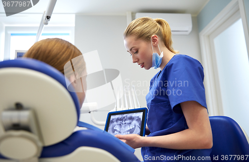 Image of dentist showing x-ray on tablet pc to patient girl