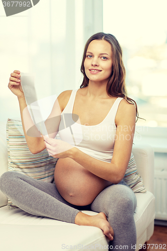 Image of happy pregnant woman with ultrasound image at home