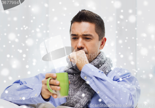 Image of ill man with flu drinking tea and coughing at home