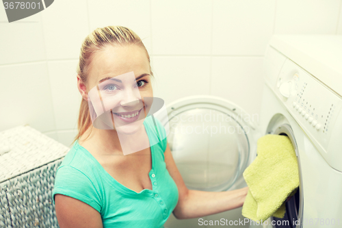 Image of happy woman putting laundry into washer at home