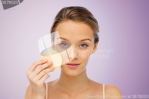 Image of young woman cleaning face with exfoliating sponge