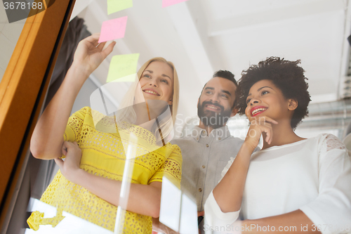 Image of happy creative team writing on stickers at office