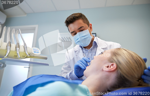 Image of male dentist in mask checking female patient teeth