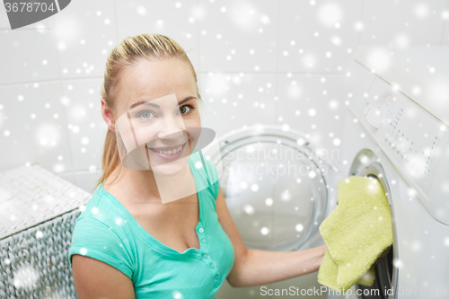 Image of happy woman putting laundry into washer at home