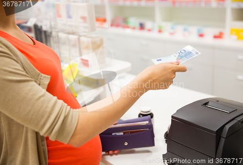 Image of pregnant woman with money at cashbox in drugstore