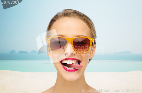 Image of happy young woman in sunglasses showing tongue