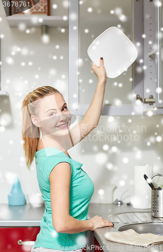 Image of happy woman putting plate to kitchen cabinet