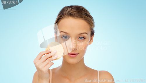 Image of young woman cleaning face with exfoliating sponge