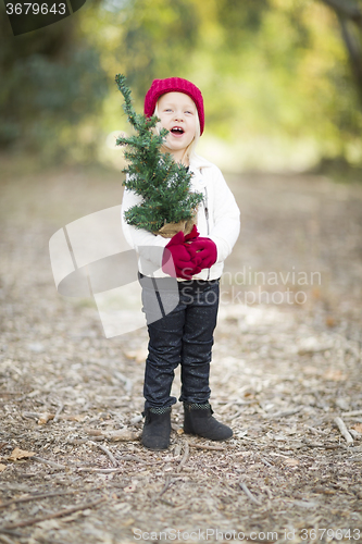 Image of Baby Girl In Red Mittens and Cap Holding Small Christmas Tree