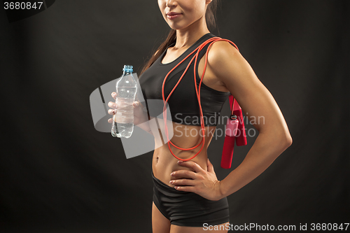 Image of Muscular young woman athlete with a skipping rope on black 