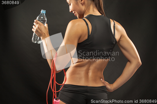 Image of Muscular young woman athlete with a skipping rope on black 