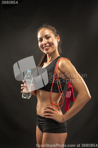 Image of Muscular young woman athlete with a skipping rope on black 