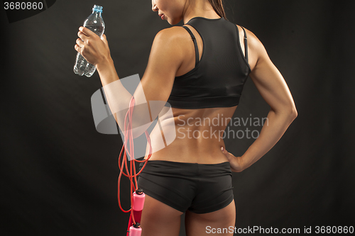 Image of Muscular young woman athlete with a skipping rope on black 